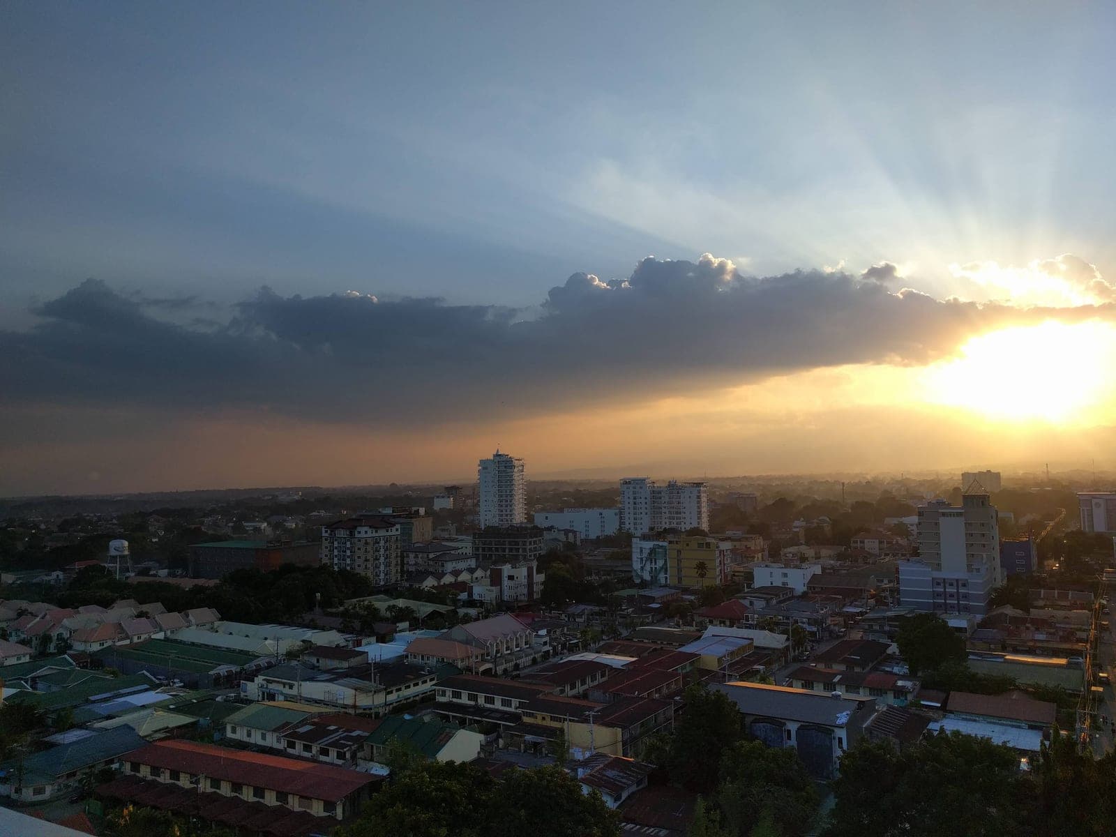 Angeles City rooftops and low-rise streets at dusk, sunbeams breaking through cloud