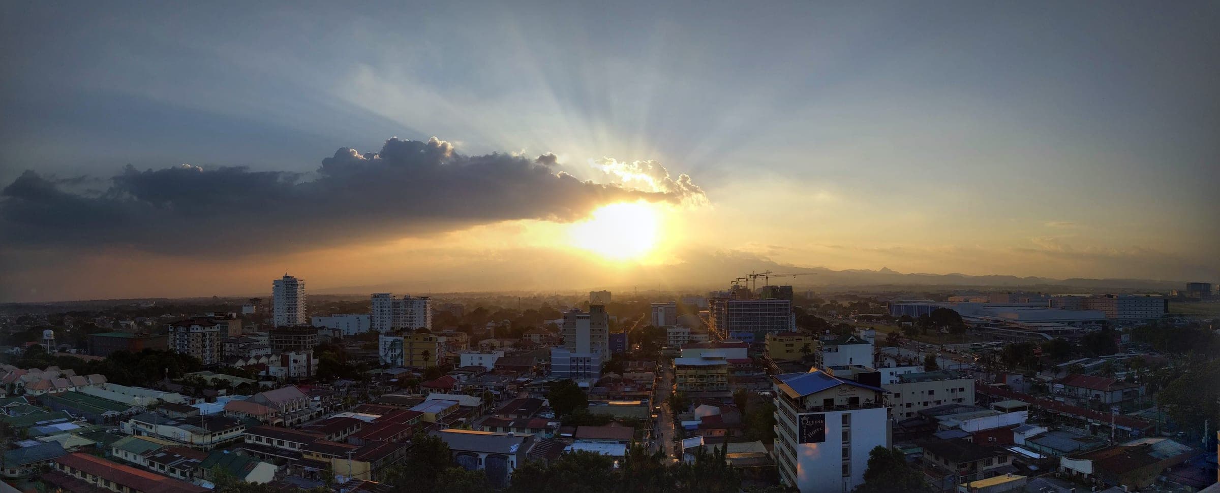Panorama of Angeles City at sunset, rooftops and hotel towers under a sunburst sky