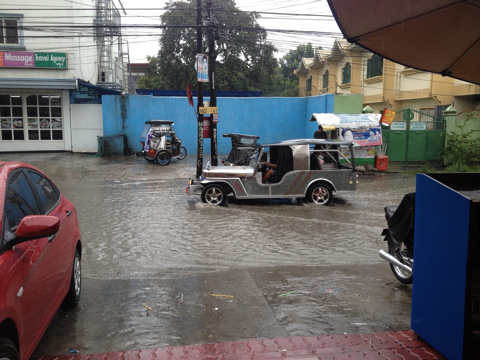 A flooded Balibago side street in Angeles City during a rainy-season downpour, a tricycle wading through