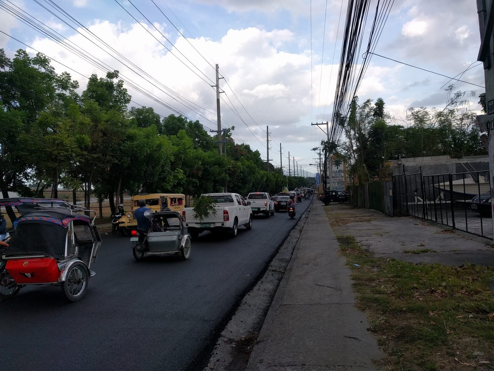 Tricycles, a jeepney and late-afternoon traffic on the road along the Clark fence, Angeles City