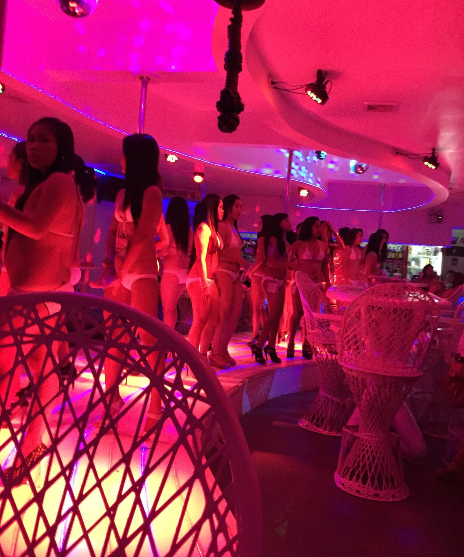 A brightly lit pink and white go-go room in Angeles City, dancers on a curved stage