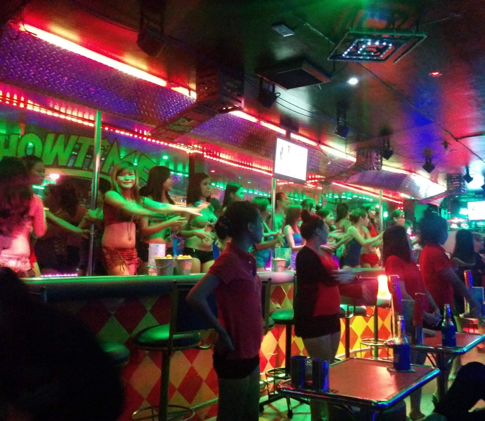 Inside an Angeles City go-go bar: dancers along the stage, neon strip lighting and a harlequin bar front